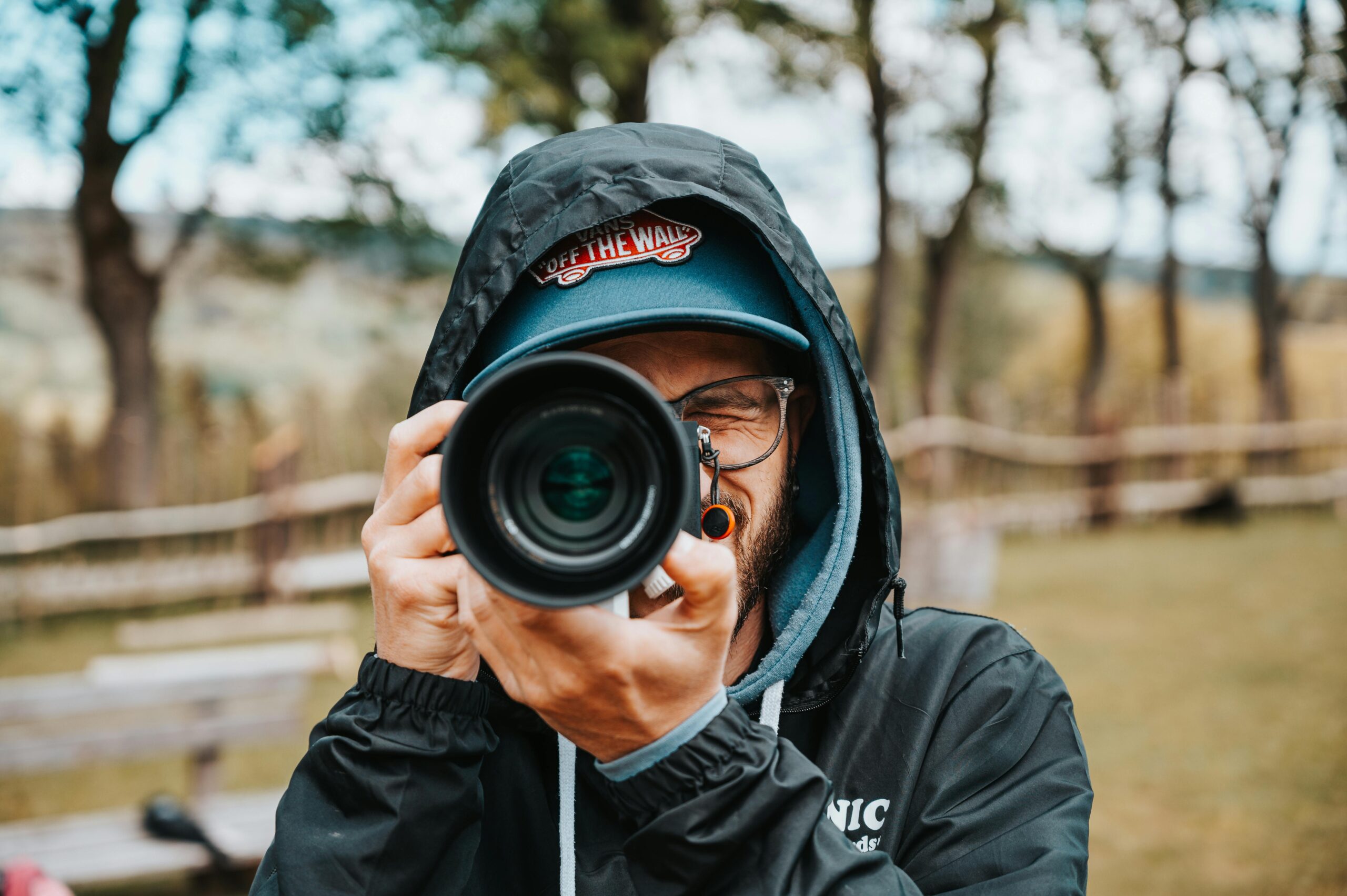 Portrait of a man outdoors capturing a moment with a camera. Focus on the camera lens and outdoor setting.